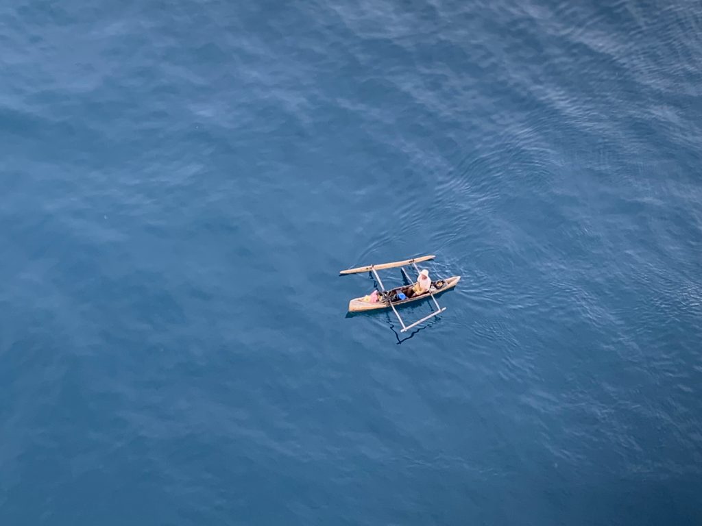 Aerial view of a single wooden outrigger pirogue crossing shallow turquoise water off the Madagascar coast