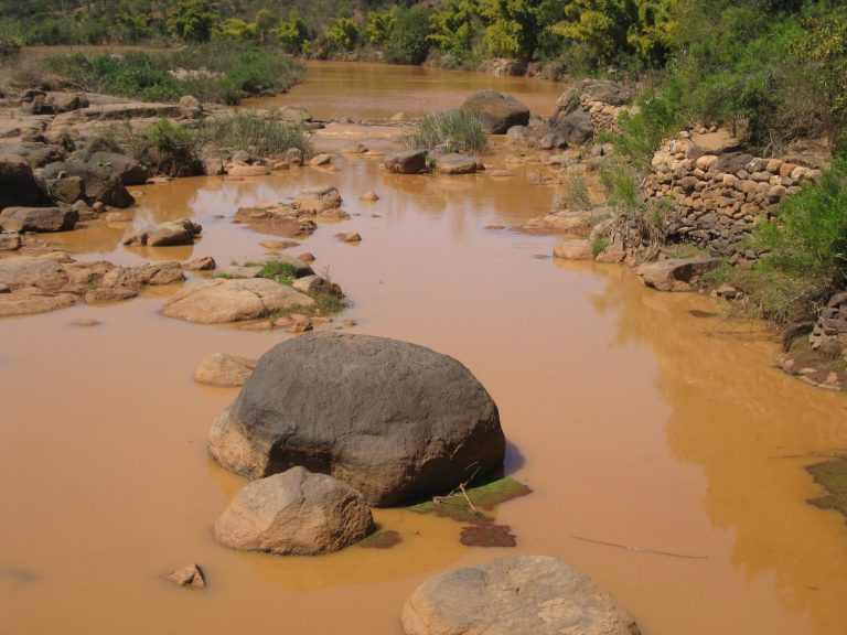 Large grey boulders breaking the surface of a fast, muddy orange river channel in Madagascar