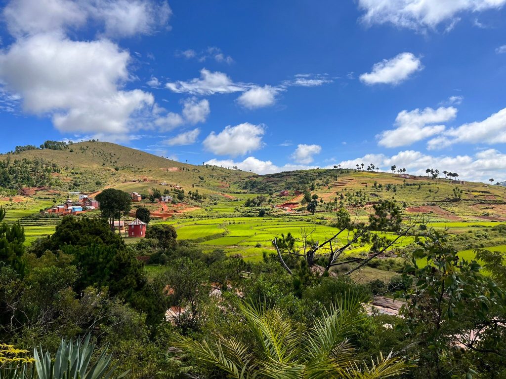 Green rice terraces stepping down a valley below a village of red brick houses in the Malagasy highlands