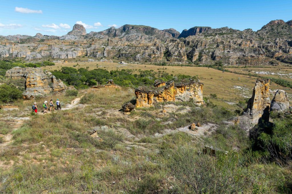 Trekkers walking a dusty trail beneath the eroded sandstone cliffs of Isalo