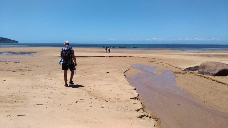 A solitary figure crossing a vast empty sandflat exposed by the low tide