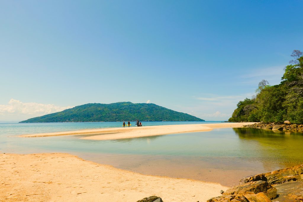 A narrow white sandbar running out to a small forested island in shallow turquoise water