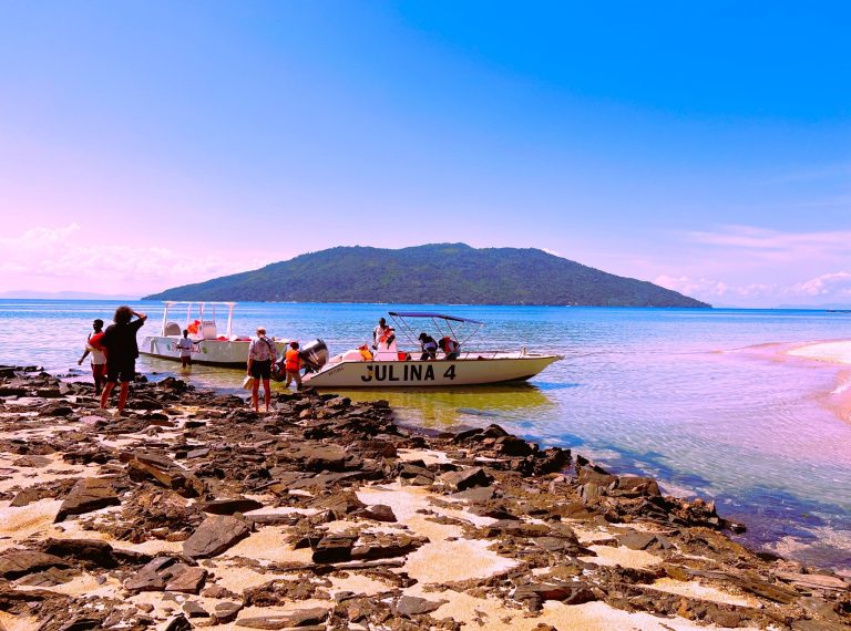 Travellers wading out to board waiting speedboats from a rocky shoreline