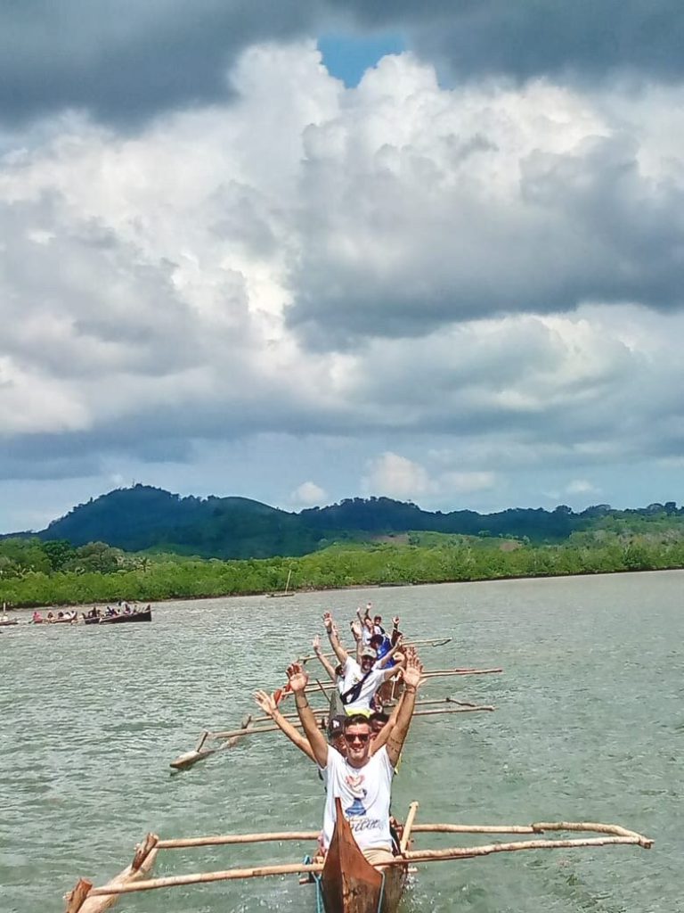 Travellers raising their arms and cheering as their outrigger pirogue crosses the bay