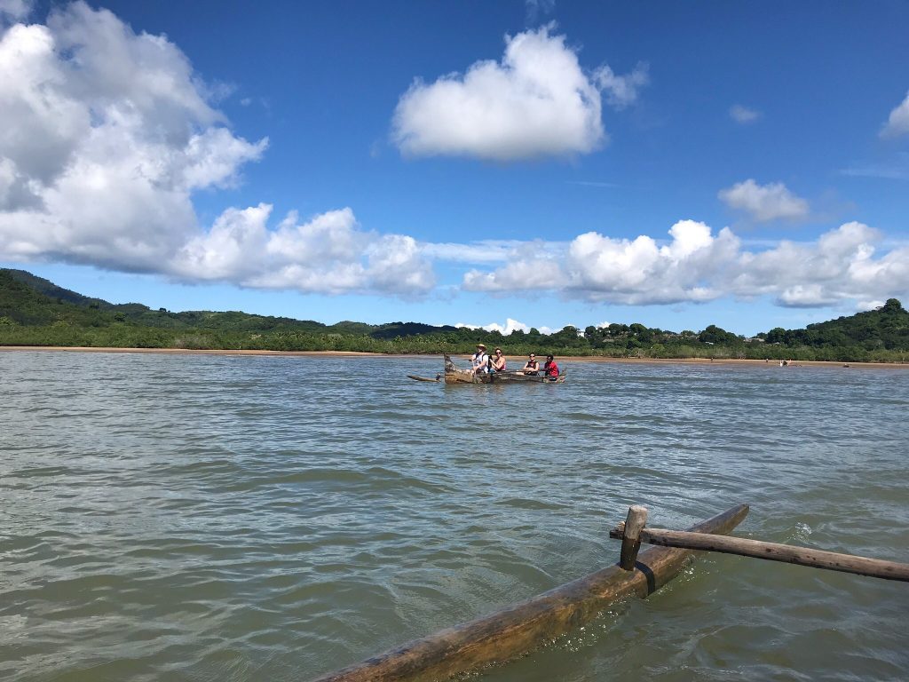 Visitors sitting low in an outrigger pirogue as it is paddled across a calm bay