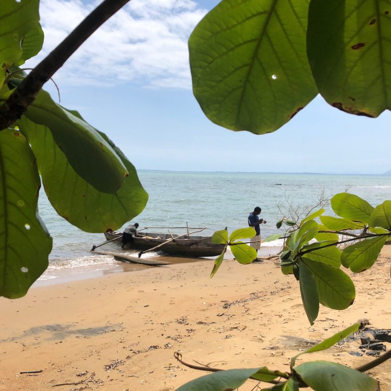 Two fishermen hauling a heavy dugout pirogue up onto the sand