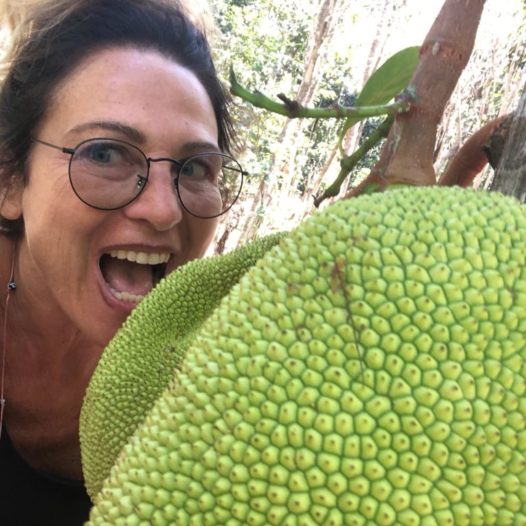 A woman laughing as she pretends to take a bite out of an enormous jackfruit